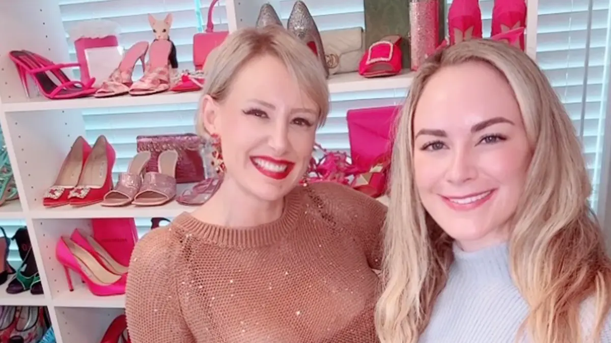 Two women smiling side by side in front of a wall of pink and red heels on the I Want Her Shoes set — the Emily Dempsey conversation about career pivots