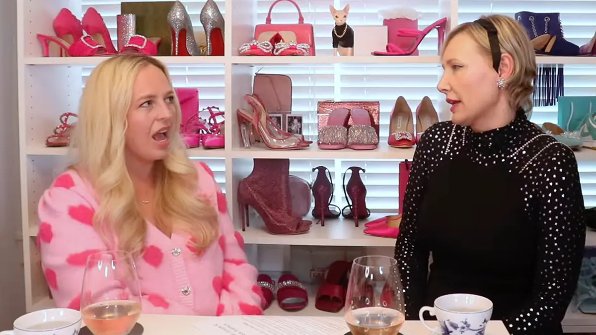 A guest in a pink-print blouse in mid-sentence opposite the host on the shoe-lined I Want Her Shoes set — the Katie Love conversation on storytelling and visibility